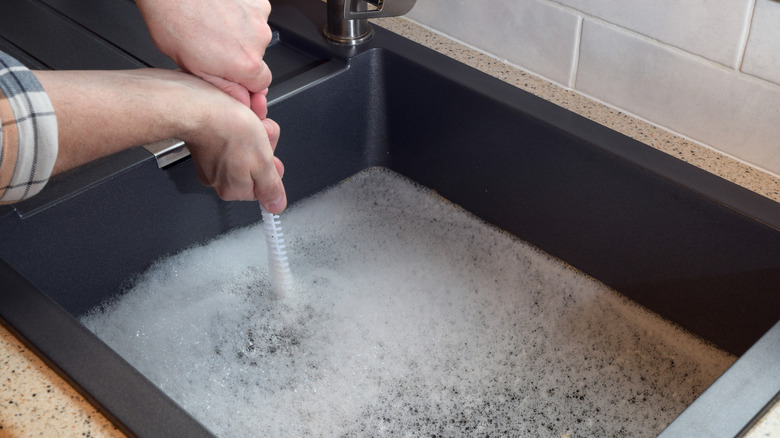 Hands trying to clear a clogged soapy kitchen sink