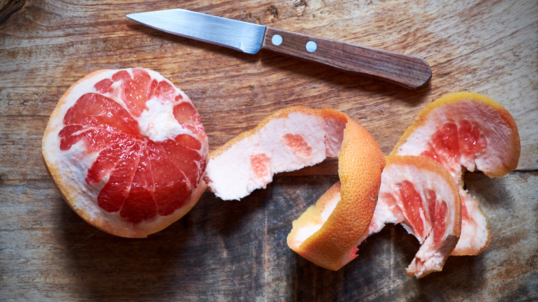 A half-peeled grapefruit on a wood cutting board.