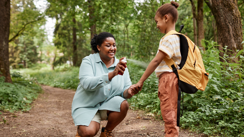 A mother protects her child with an anti-fly spray while hiking in the woods