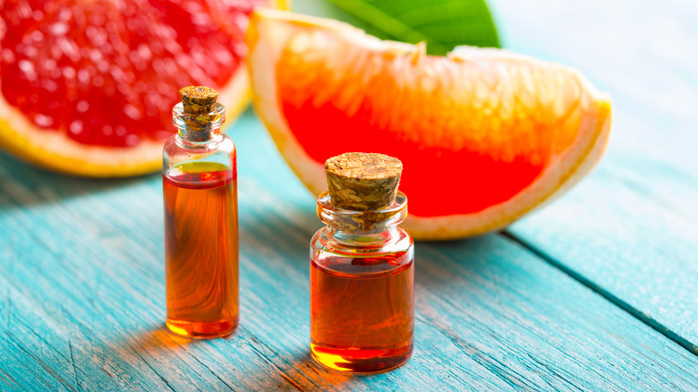 Two glass bottles of grapefruit oil with cork stoppers sitting on a wooden teal table in front of two slices of grapefruit
