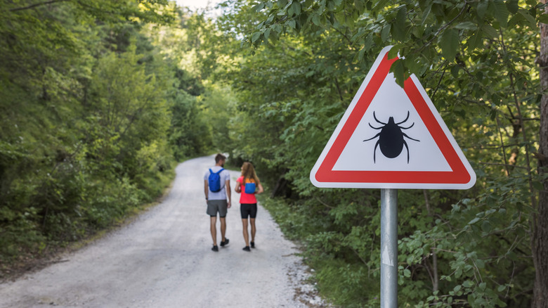 Couple hiking on a path past a tick warning sign