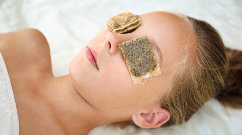 Young woman laying down with tea bags on her eyes
