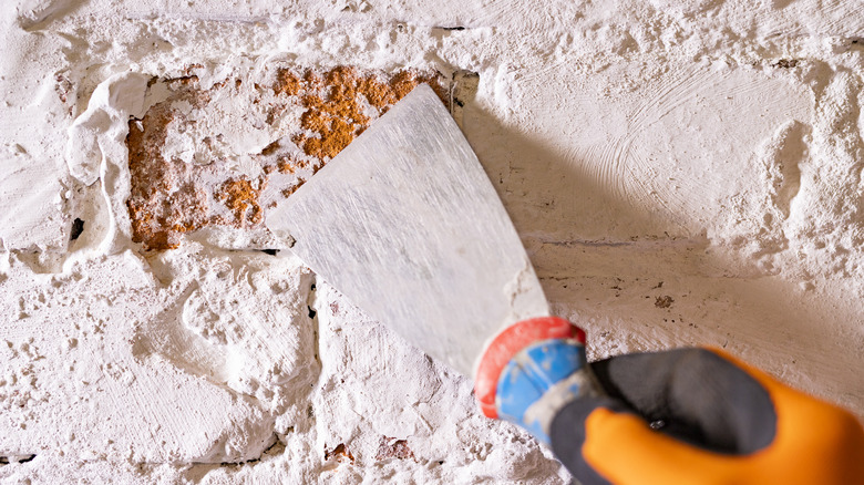 Person removing old paint on a brick wall using a scraper