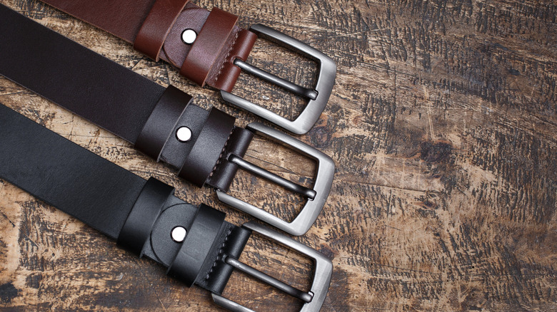 Buckle ends of three leather belts on a wooden surface