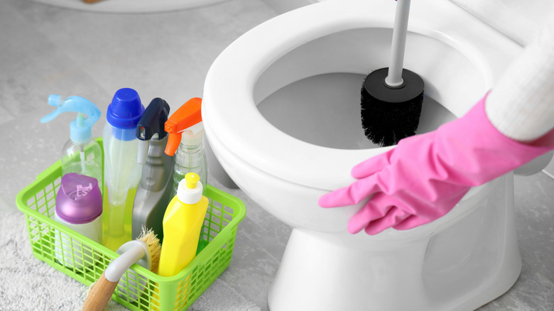 Person using brush to scrub toilet with cleaning products on floor