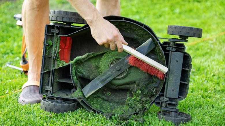 Someone cleaning the underside of lawn mower with a brush