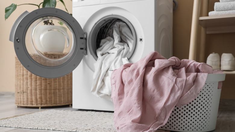 Interior of laundry room with washing machine, bed sheets, and basket