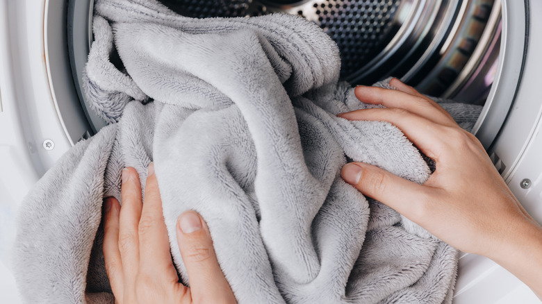 Close-up of hands putting a gray towel into a laundry machine
