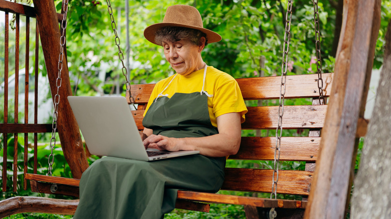 Woman in gardening clothes using laptop outdoors