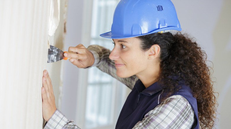 carpenter using wall scraper to remove wallpaper
