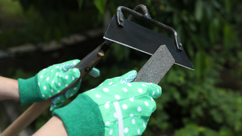 person sharpening a garden hoe with a sharpening file