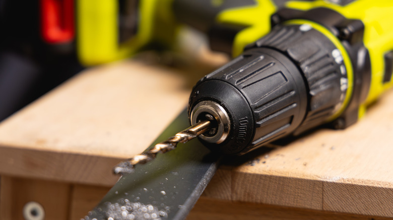 A bright yellow drill with a dull drill bit sits on a wood table.