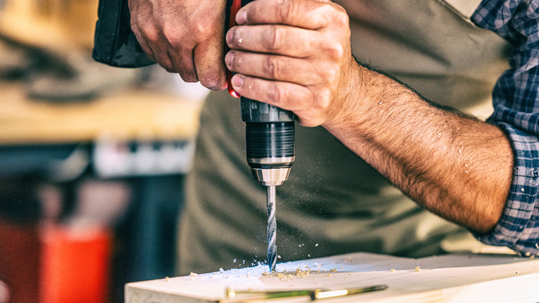 A man using electric drill on a wood piece