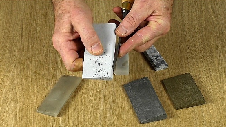 A person using a white slip stone to sharpen a wood carving tool