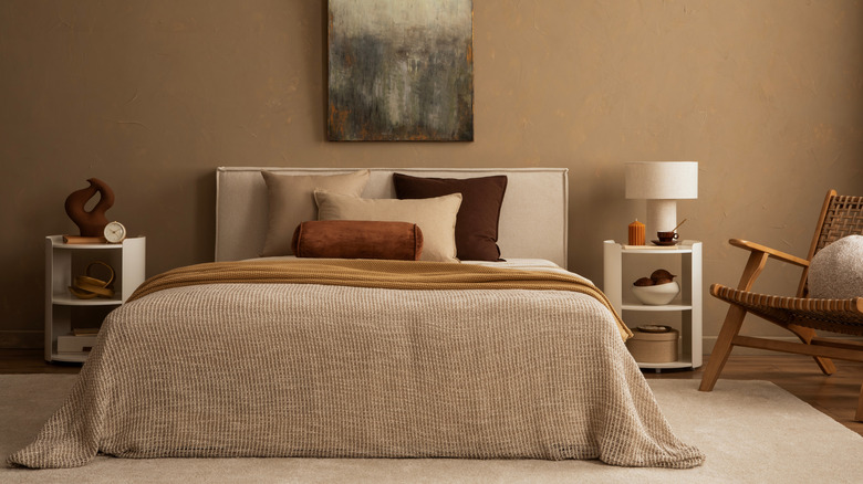 Warm colored bedding with a comforter, throw blanket, and throw pillows in a neutral bedroom