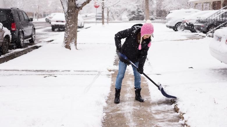 A woman in a pink hat pushes snow off a walkway