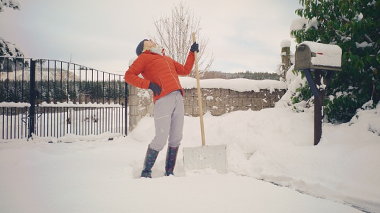 A woman holds a snow shovel while bending backwards