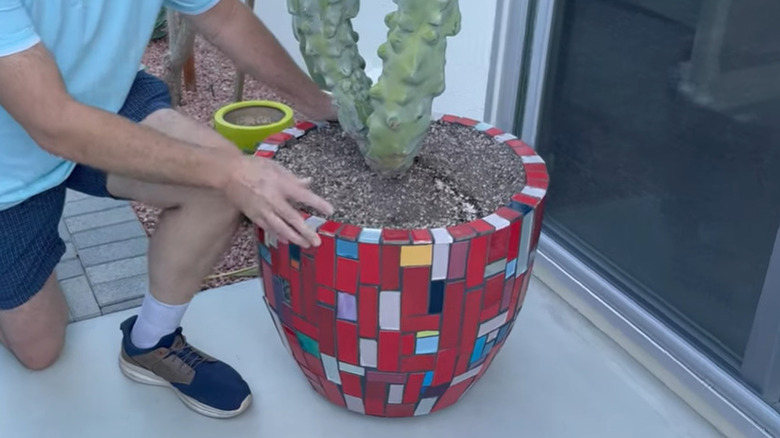 A man kneeling next to a mid-century modern mosaic planter on a patio.