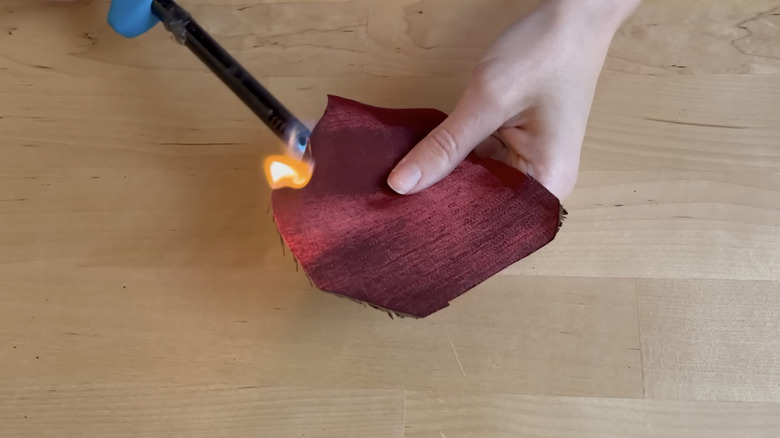 Woman does the burn test on a dark red piece of fabric.