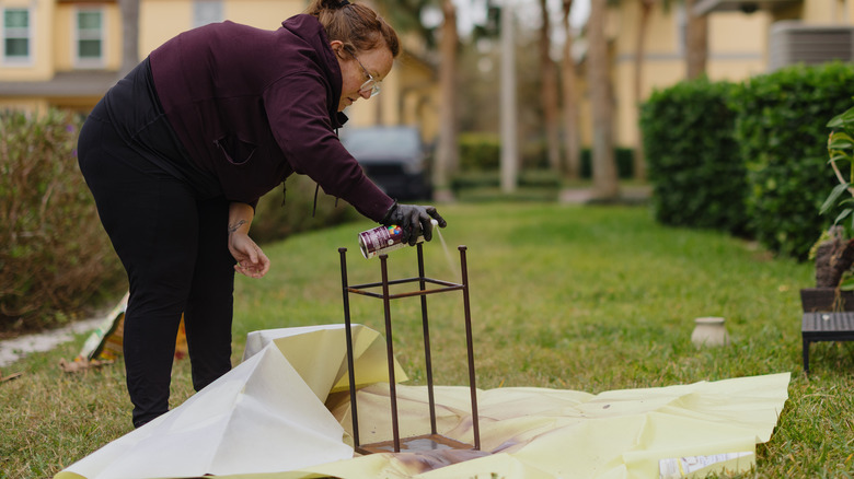A woman spray painting an upturned piece of furniture