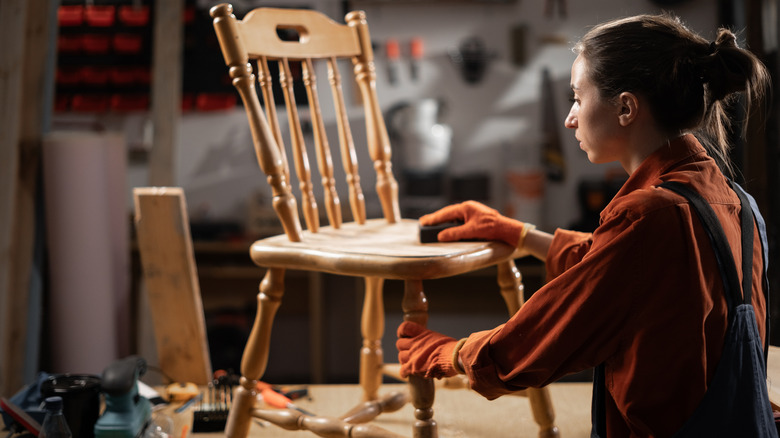 Woman sanding wood chair in workshop