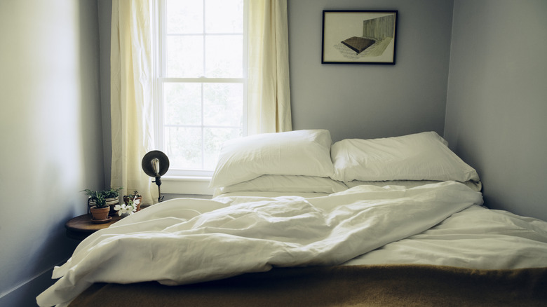 A bedroom with gray walls, a bed covered in white sheets, and an off-center window