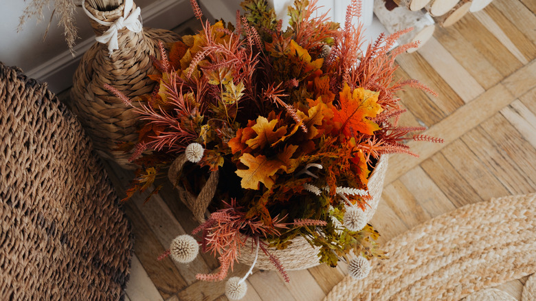 A fall basket on the floor near a fireplace with foliage and other dried and faux picks