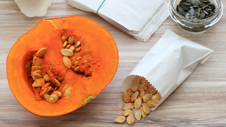 A pumpkin with seeds and some dried pumpkin seeds in a paper bag