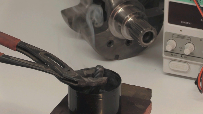 a person dips a heated bolt in a cup of oil