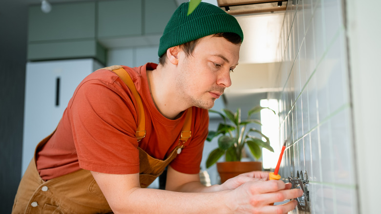 A person adjusting an outlet so the mounting brackets are placed on a tile backsplash