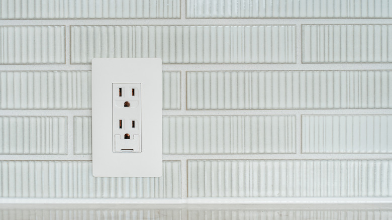 A white kitchen tile backsplash with an electrical outlet