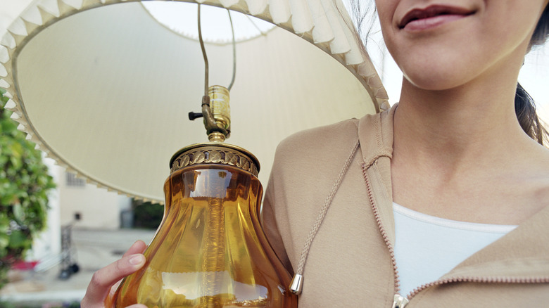 A person caries a vintage lamp with a clear amber-colored glass base