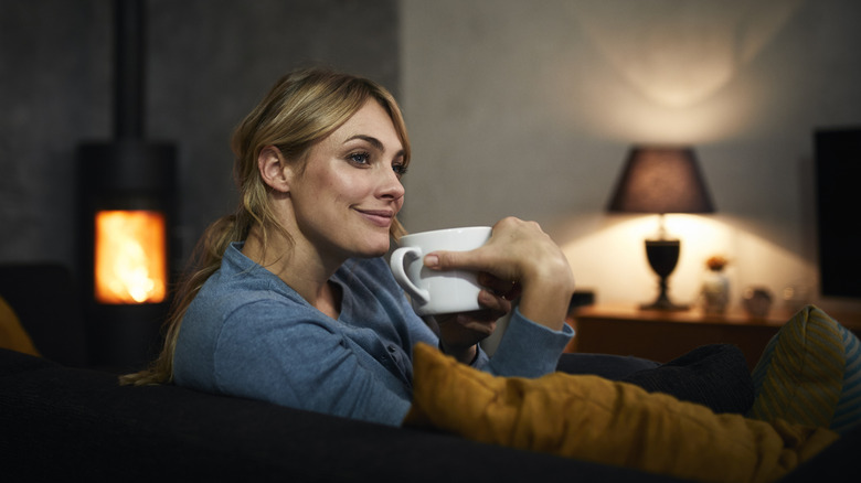 smiling woman with coffee mug sitting in room with too little lighting and gloomy dark corners