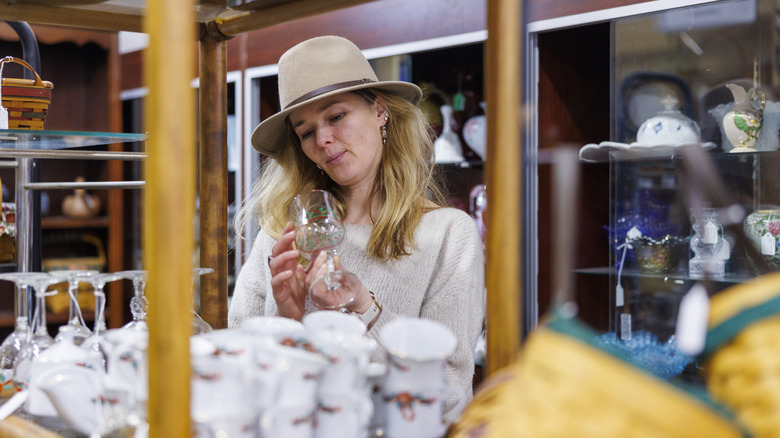 A person wearing a tan hat examining glassware at an antique store