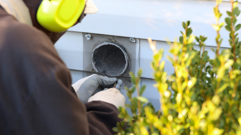 A technician servicing a dryer exhaust vent outside the home