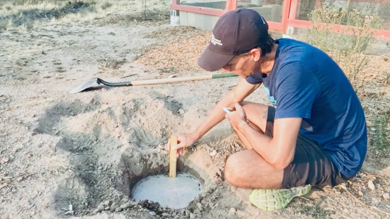 Man performs percolation test by placing ruler in hole filled with water.