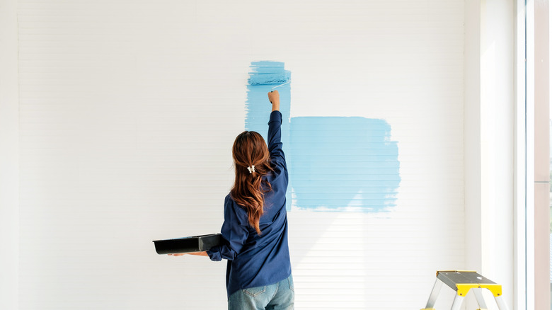 Woman using a roller to paint a white wall blue