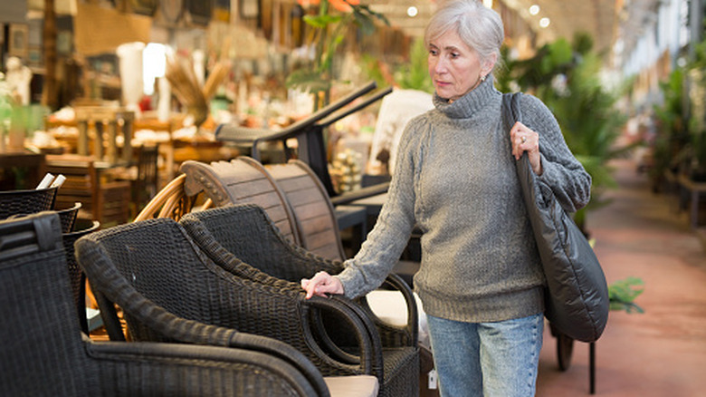 An older woman looking at black wicker furniture in  store