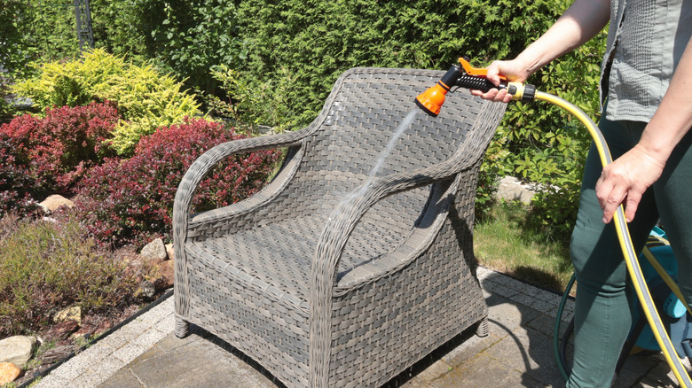 A person wit a hose spraying down what is likely syntetic wicker furniture