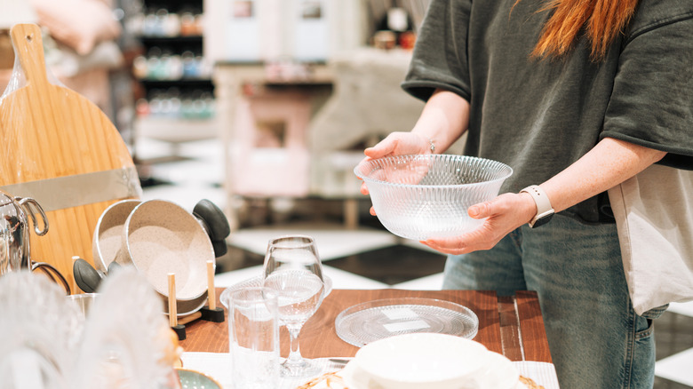 A woman with long hair holds a glass bowl, examining it to determine whether to purchase it.