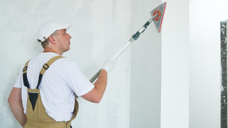 person sanding drywall with pole