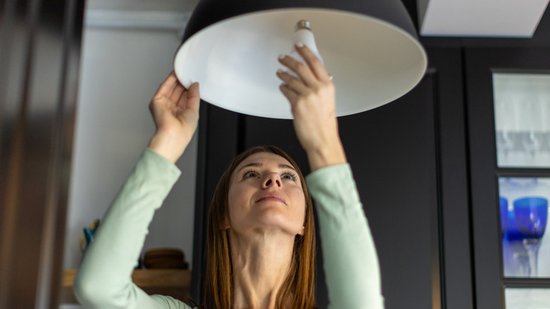 Woman tightens an LED lightbulb in hanging pendant light