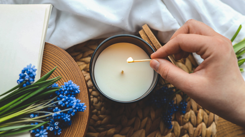 A person lights a candle, which is resting on a wicker table,  using a match