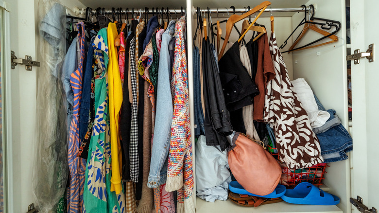 A messy, overfilled clothing storage area with loose clothing on hangers