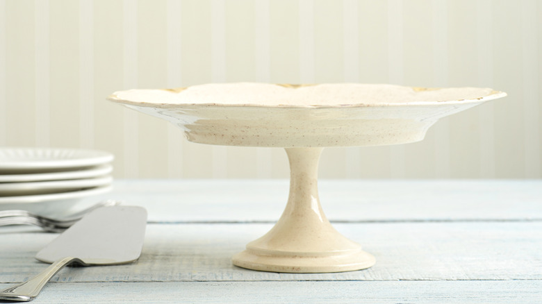 An old cake stand with nothing on it, sitting on a table next to plates and cake server.