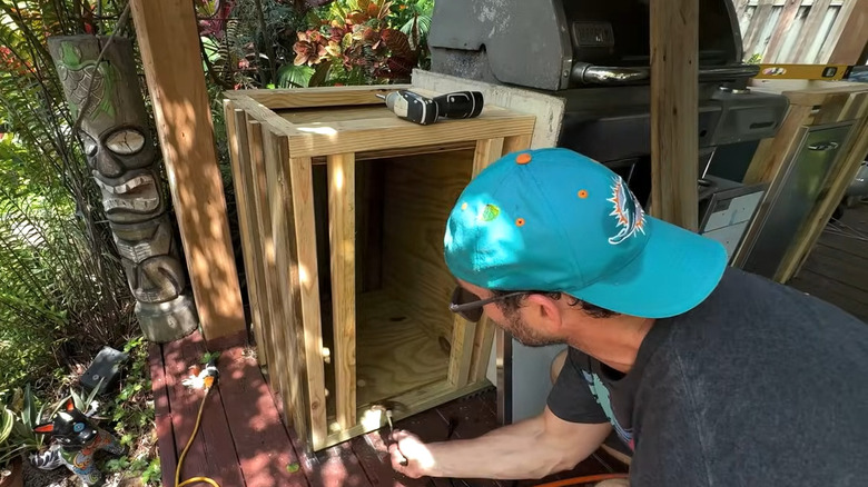 A man in a blue hat, building a wood frame around a grill.