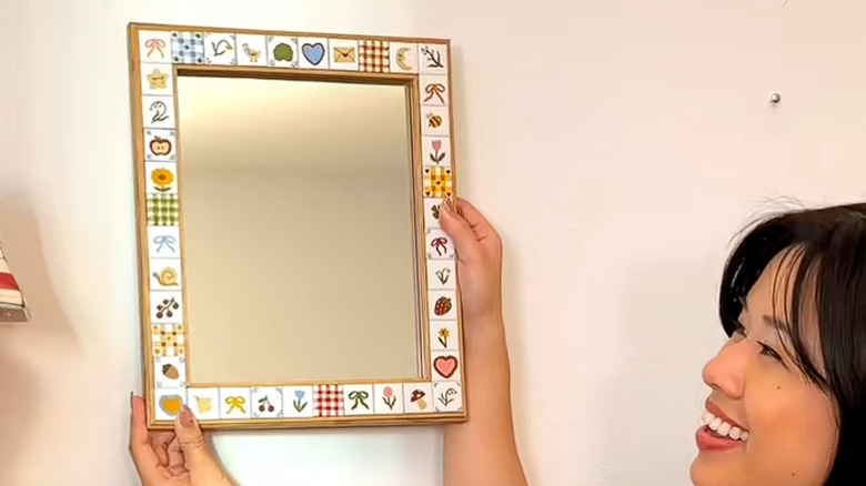 A woman holding up her hand painted tile mirror DIY