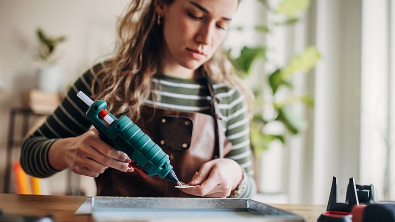 A woman hot gluing the back of a metal frame