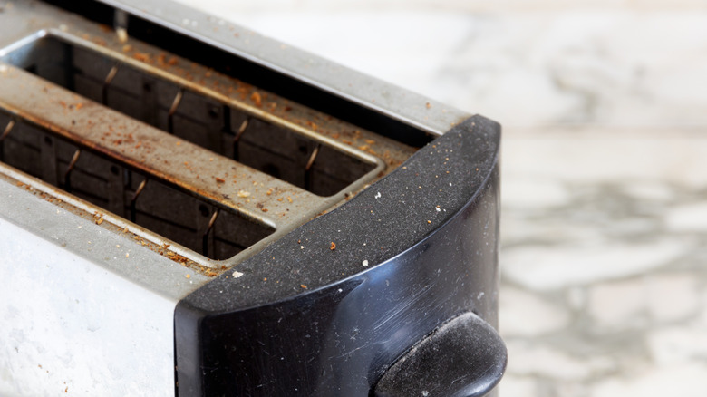 An old, rusty, dirty toaster sits on a marble counter