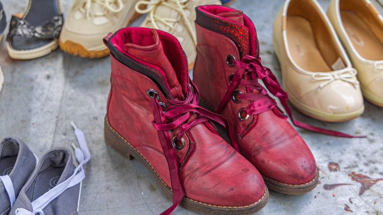Five pairs of shoes on a messy floor with red boots in the center